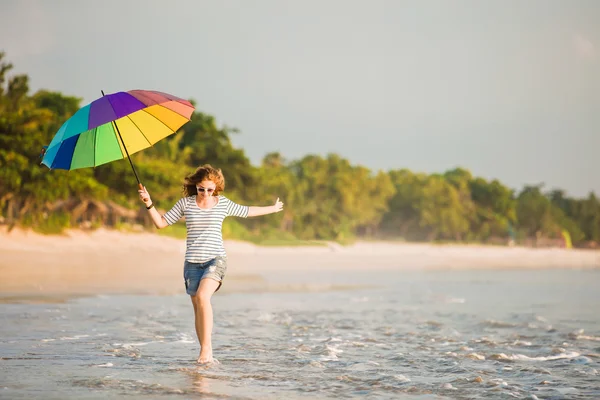 Vidám fiatal lány szivárvány esernyő szórakozás a strandon naplemente előtt. utazás, üdülés, nyaralás, egészséges életmód fogalma — Stock Fotó