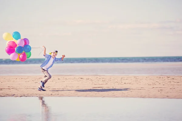 Glücklicher Junge spielt mit bunten Luftballons am Strand — Stockfoto