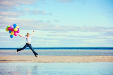 Beautiful girl jumps on the beach while holding colored balloons clipart
