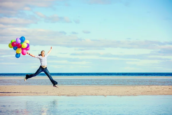 Beautiful girl jumps on the beach while holding colored balloons — Stock Photo, Image