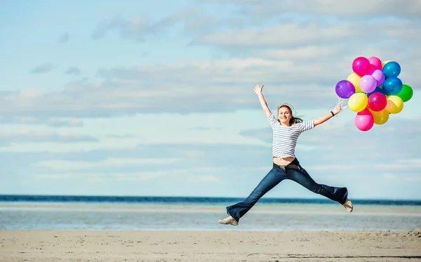 Όμορφο κορίτσι άλματα στην παραλία κρατώντας χρωματιστά μπαλόνια — Φωτογραφία Αρχείου