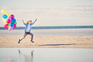 Mutlu çocuk renkli balonlarla sahilde çalış.