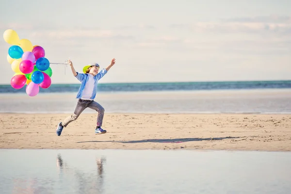 Lycklig pojke leker med färgade ballonger på stranden — Stockfoto