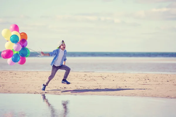 Garçon heureux joue avec des ballons colorés sur la plage — Photo