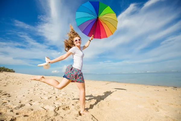 Jovencita alegre con paraguas de arco iris divertirse en la playa —  Fotos de Stock