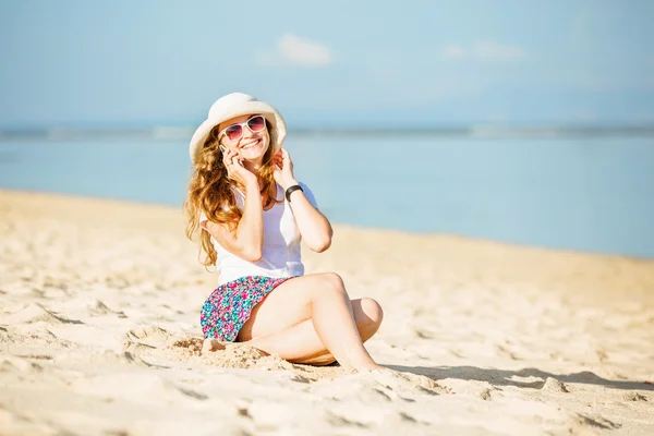 Красивая молодая женщина на пляже разговаривает по мобильному телефону и смеется — стоковое фото