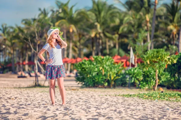 Beautiful young caucasian woman at the beach in white hat talking on mobile phone and laughing — Zdjęcie stockowe