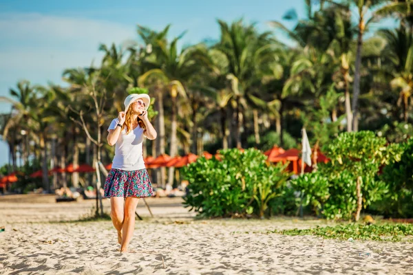 Hermosa joven mujer caucásica en la playa en sombrero blanco hablando por teléfono móvil y riendo —  Fotos de Stock