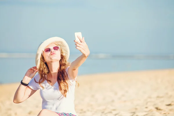Beautiful young woman on the beach at sunny day taking selfie with phone — Stock Photo, Image