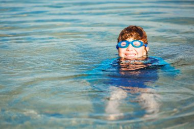 Happy smiling boy with goggles on swim in shallow water
