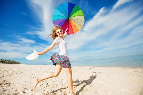 Cheerful young girl with rainbow umbrella having fun on the beach