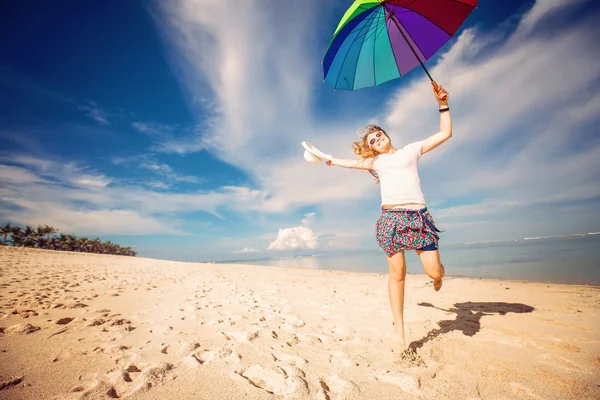 Jovencita alegre con paraguas de arco iris divertirse en la playa — Foto de Stock