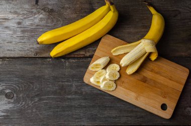 Ahşap kesme tahtasında dilimlenmiş muz, ahşap arka planda yemek pişirmeye hazırlanıyor..