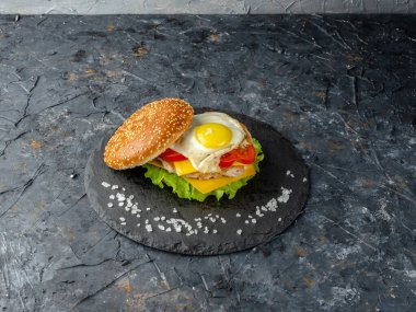 Koyu beton bir arka planda tahta üzerinde yumurtalı hamburger.