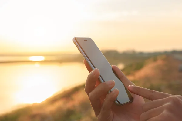 Крупним планом рука використовує телефон на відкритому повітрі під час заходу сонця — стокове фото