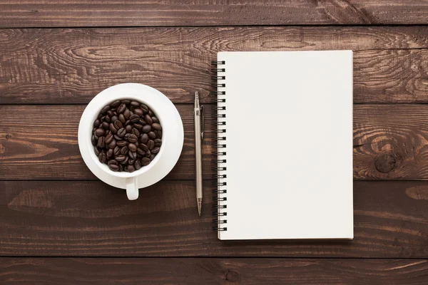 Kávová zrna v poháru a kniha prázdné stránky na dřevěný stůl — Stock fotografie