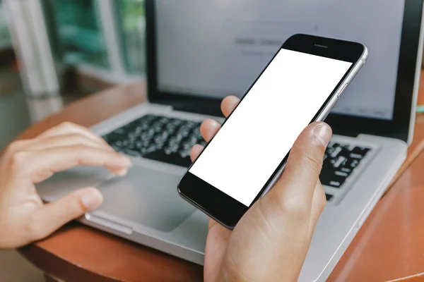 Hand holding phone and using laptop computer in coffee shop — Stock Photo, Image