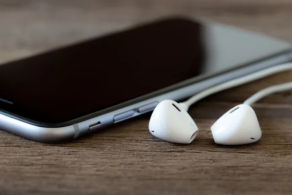 Closeup phone and earbud on wood desk — Stock Photo, Image