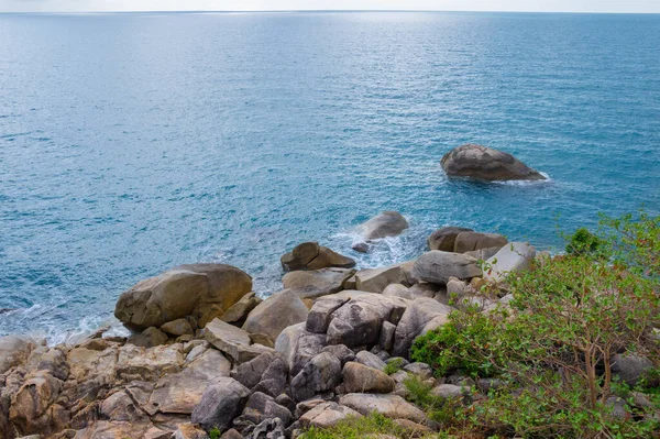 Top view from the cliff towards the sea rocks and surf with waves at Kph Samui island, Thailand. Beautiful blue water waves against rocky shore