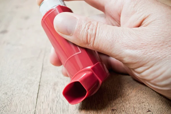 Closeup of asthma aerosol in hand on wooden table background — Stock Photo, Image