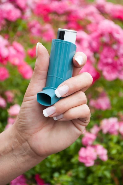 Closeup of hand of woman with asthma aerosol in outdoor near pink flowers — Stock Photo, Image