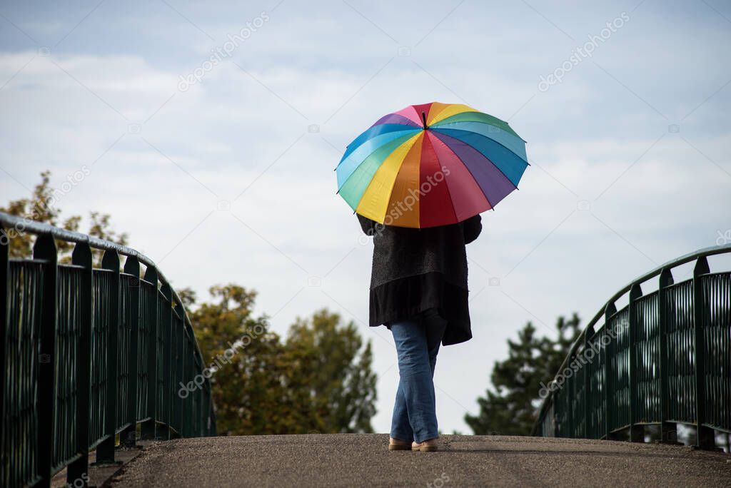 Portrait on back view of woman standing with a rainbow umbrella on bridge