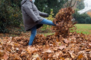 Halka açık bir bahçede sonbahar yapraklarıyla oynayan kadın portresi