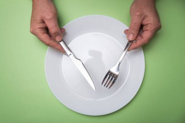 Kadının elleri yeşil arka planda boş tabağında.