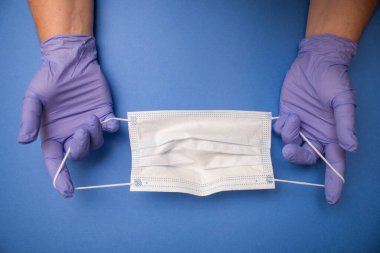 Lateks eldivenli bir adam mavi arka planda tıbbi maske takıyor.