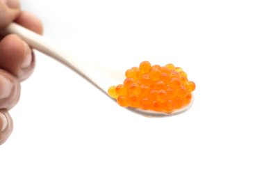 Beyaz arka planda beyaz seramik kaşıkta alabalık yumurtalarının yakın çekimi