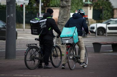 Strasbourg - Fransa - 4 Şubat 2021 - Delveroo ve Uber 'in arka plandaki portresi sokakta bisikletli teslimatçıları yiyor