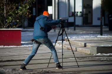 Arka planda, sokakta tripodla fotoğraf çeken bir adamın portresi. 