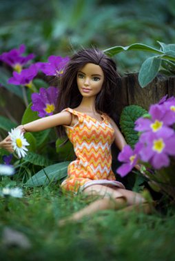 Mulhouse - Fransa - 31 Mart 2021 - Turuncu elbise giyen esmer Barbie bebek halk bahçesinde oturuyor