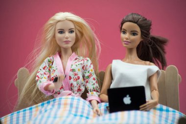 Mulhouse - Fransa - 16 Nisan 2021 - Yatakta pembe arka planda elma bilgisayarıyla oturan sarışın ve esmer Barbie bebeklerin portresi