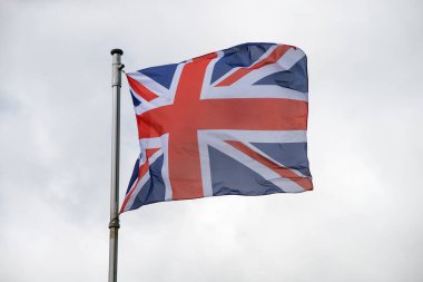 Gri gökyüzü arka planında sallanan İngiliz bayrağının yakın çekimi