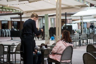Colmar - Fransa - 21 Mayıs 2021 - Covid-19 pandemisi sırasında restoran terasındaki garson ve yüz maskeli müşterilerin portresi 