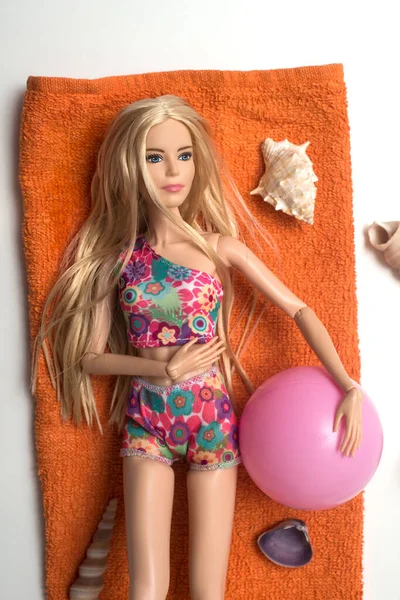 2021年5月26日 穿着彩色比基尼的金发芭比娃娃躺在橙色浴巾上 背景为白色海贝壳的肖像 — 图库照片