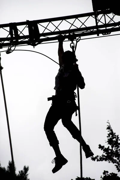 Silhouette of girl climbing on metallic structure on cloudy sky background