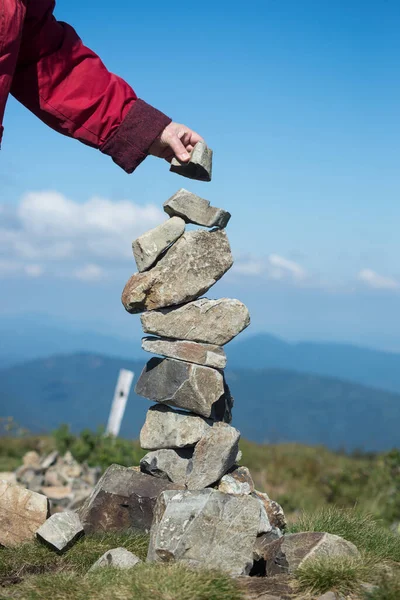 在蓝天背景的山顶上做石头平衡的女人的手的被子 — 图库照片