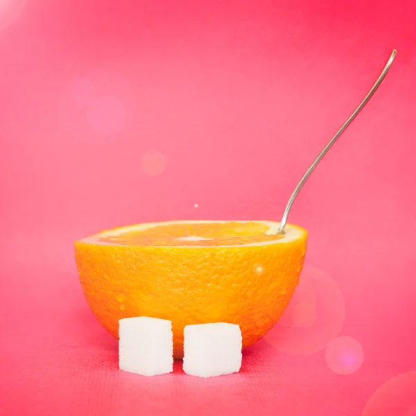 Апельсин с ложкой и сахаром на розовом фоне — стоковое фото
