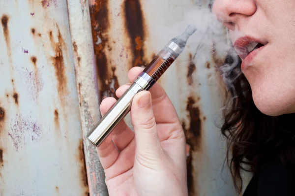 Kvinna med e-cigarett på rost bakgrund — Stockfoto