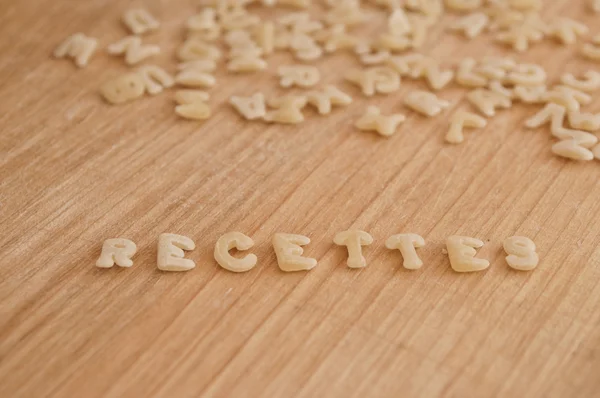 Pasta del alfabeto que forma el texto "recettes" (recibos en francés) sobre fondo de madera — Foto de Stock