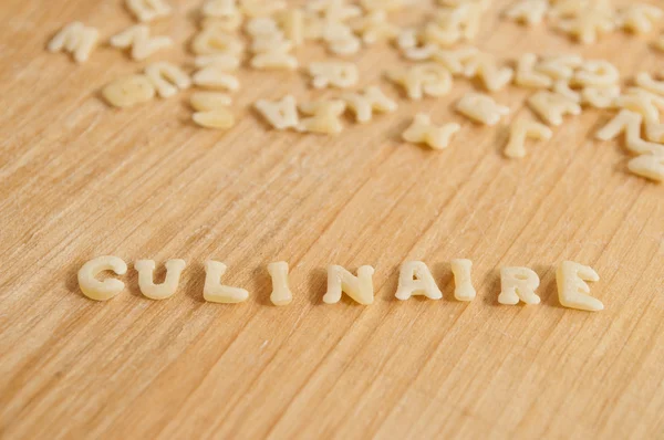 Alphabet pasta forming the text "culinaire" (culinary in french) on wooden background — Stock Photo, Image