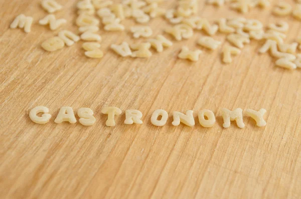 Pasta del alfabeto que forma el texto "gastronomía" sobre fondo de madera — Foto de Stock