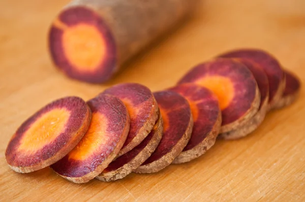 Primer plano de zanahorias violetas en rodajas sobre tabla de cortar de madera —  Fotos de Stock