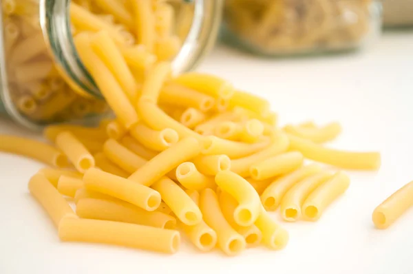 Primer plano de la pasta que cae del recipiente de vidrio sobre fondo blanco — Foto de Stock