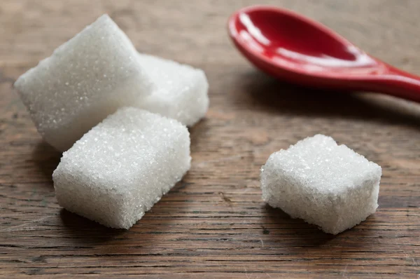 Gros plan de cubes de sucre avec une cuillère rouge sur fond en bois — Photo