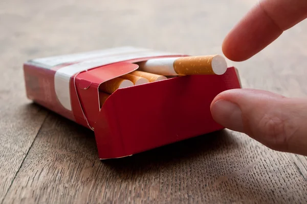 Primer plano del hombre que está tomando un cigarrillo de paquete de cigarrillos en el fondo de madera — Foto de Stock