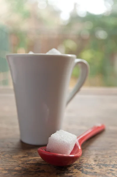 Nahaufnahme eines Zuckerwürfels in einem roten Löffel auf hölzernem Hintergrund — Stockfoto