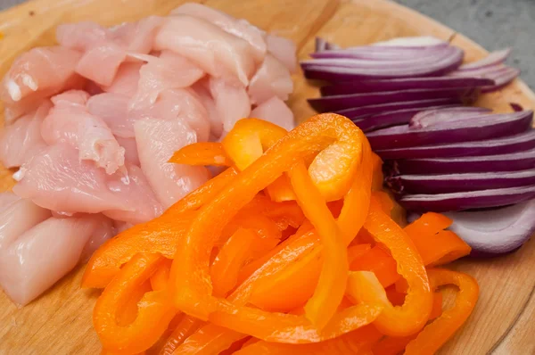 Chicken breast orange pepper and onions on wooden cutting board — Stock Photo, Image